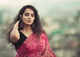 A beautiful South Asian woman wearing a vibrant saree with a blurred cityscape backdrop.