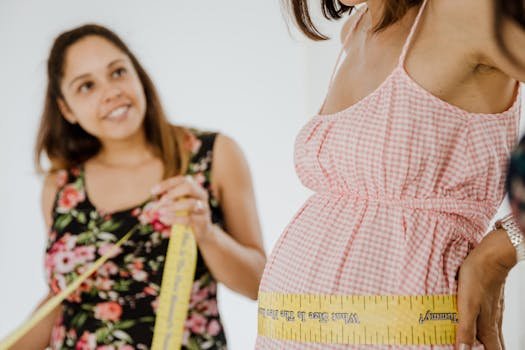 A pregnant woman measures her belly with a tape measure assisted by a friend.